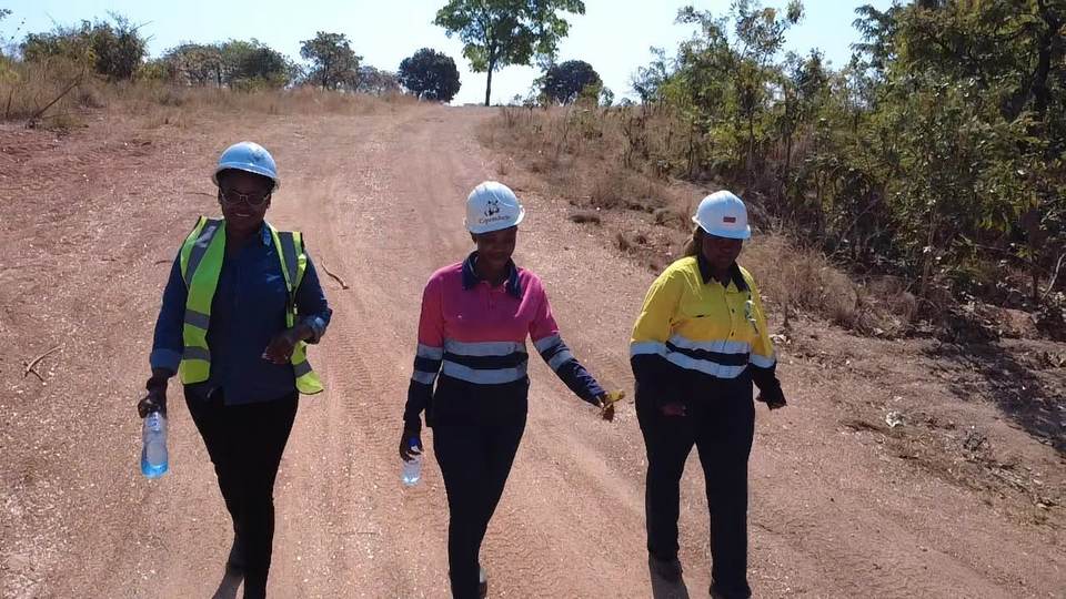 Three women of the Cipembele team in hard hats and high-visibility workwear walking on site
